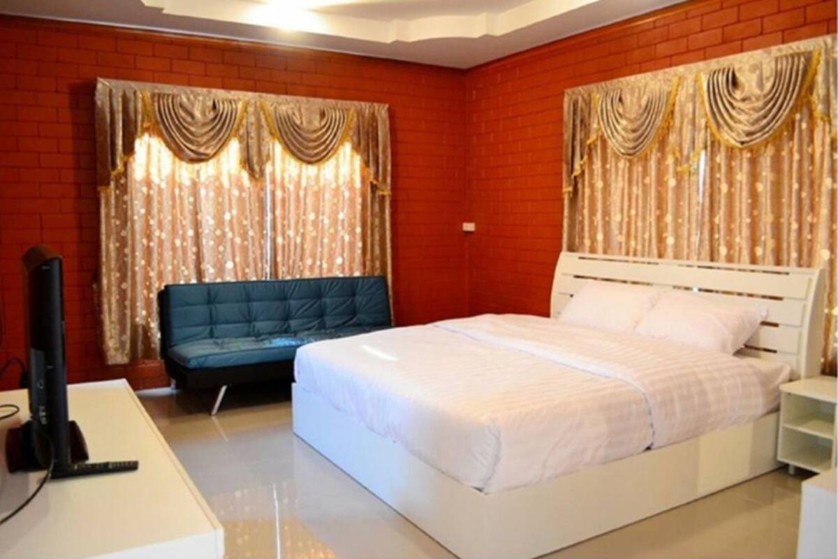A bedroom with a white bed, a blue sofa, and curtains with gold trim.