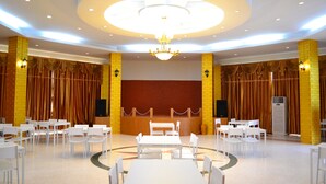 Un grand hall doté d’une table centrale entourée de chaises, de murs en briques jaunes et d’un lustre.