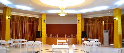 A spacious hall with a central table surrounded by chairs, yellow brick walls, and a chandelier.