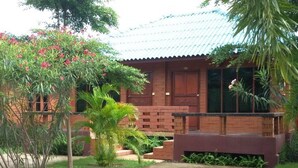 Une maison traditionnelle en bois, avec un toit en tuiles, entourée d’une végétation luxuriante et d’un jardin bien entretenu.