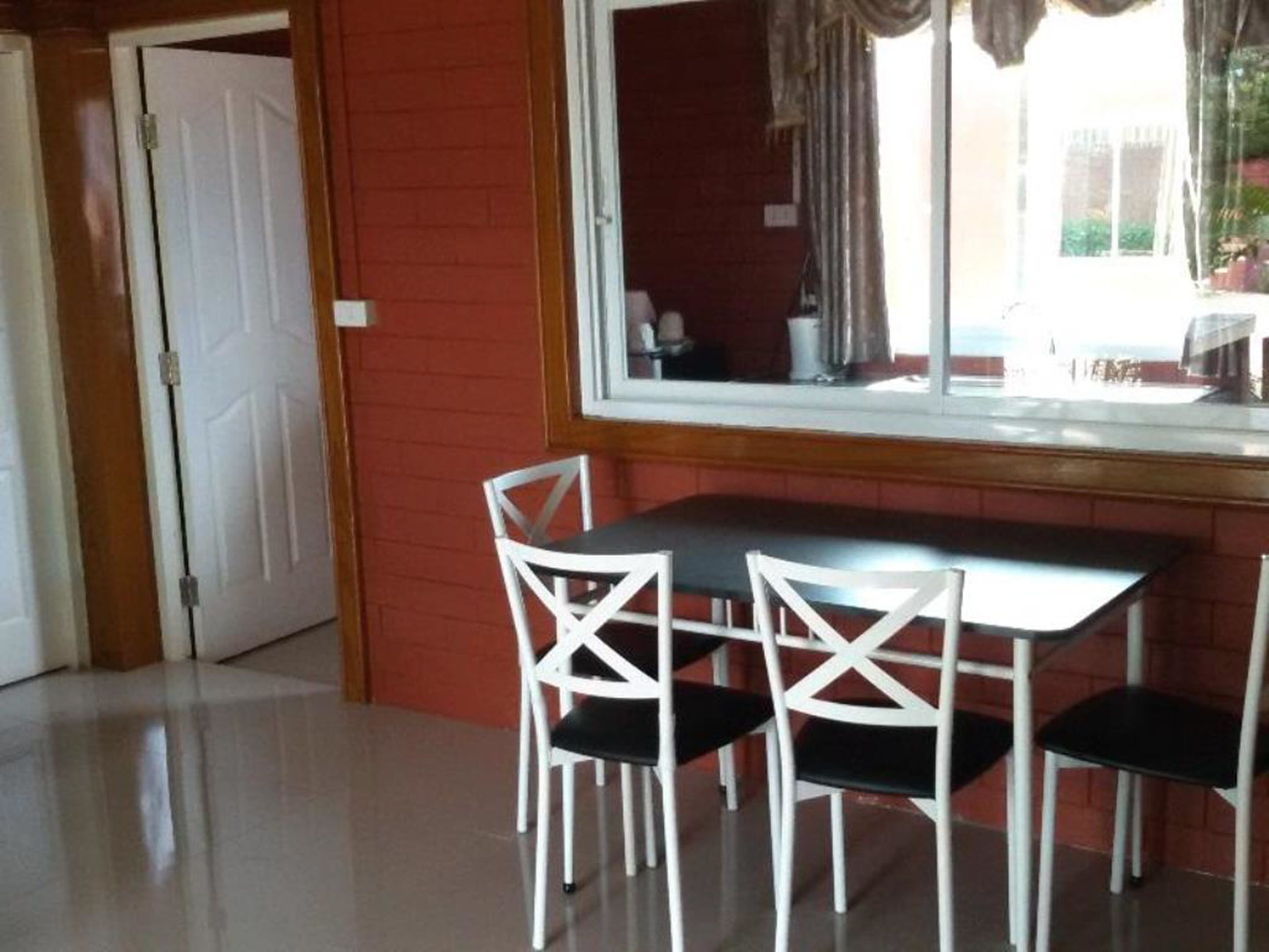 Un comedor con una mesa y cuatro sillas blancas, una ventana con cortinas y una pared de ladrillo rojo.