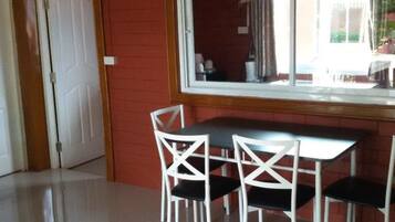 Un comedor con una mesa y cuatro sillas blancas, una ventana con cortinas y una pared de ladrillo rojo.