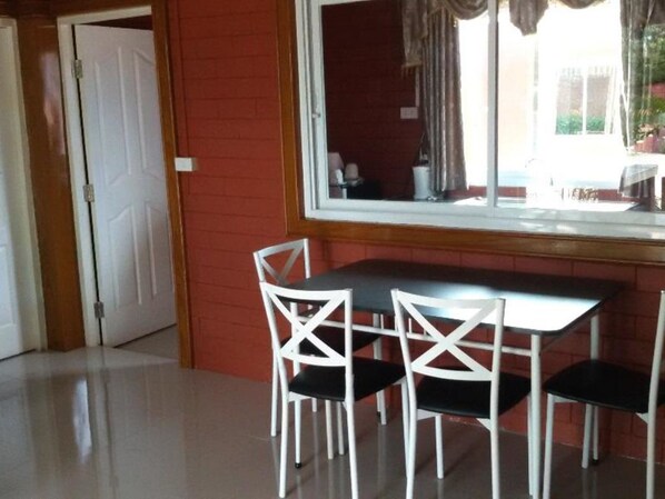 A dining area with a table and four white chairs, a window with curtains, and a red brick wall.