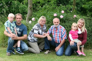 Una familia de cinco personas en un jardín, con follaje y flores al fondo.