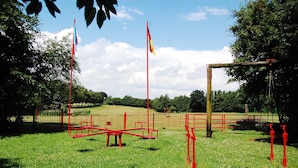 A park with red playground equipment, a flagpole, and a wooden structure. - Vacation apartment Stör - Ferienhof Röhling between Schlei and Baltic Sea (Kappeln)
