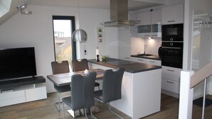 Cocina moderna con una isla central, electrodomésticos integrados y un área de comedor con televisor y asientos.