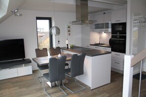 A modern kitchen with a central island, built-in appliances, and a dining area with a TV and seating.