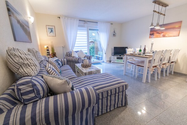 Una sala de estar con un sofá a rayas, una mesa de comedor con sillas y un televisor.