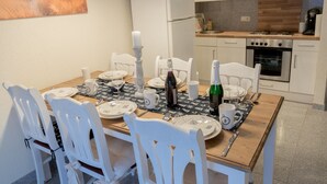 Un coin repas avec une table en bois dressée pour quatre personnes, des chaises blanches et des luminaires suspendus.