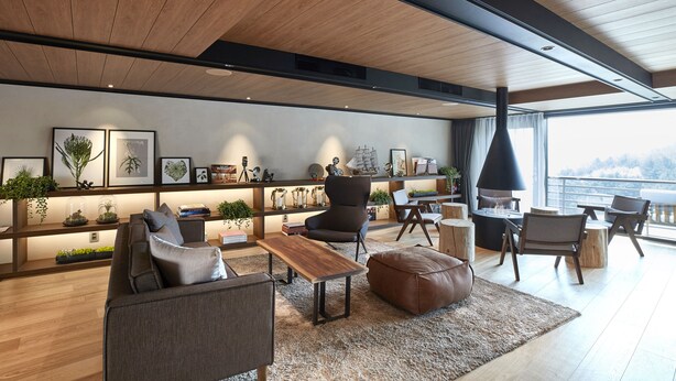 A modern living room with a wooden ceiling, a large window with a view, a bookshelf with decorative items, and a seating area with a sofa and chairs. - Walkerhill Douglas House (Seoul)