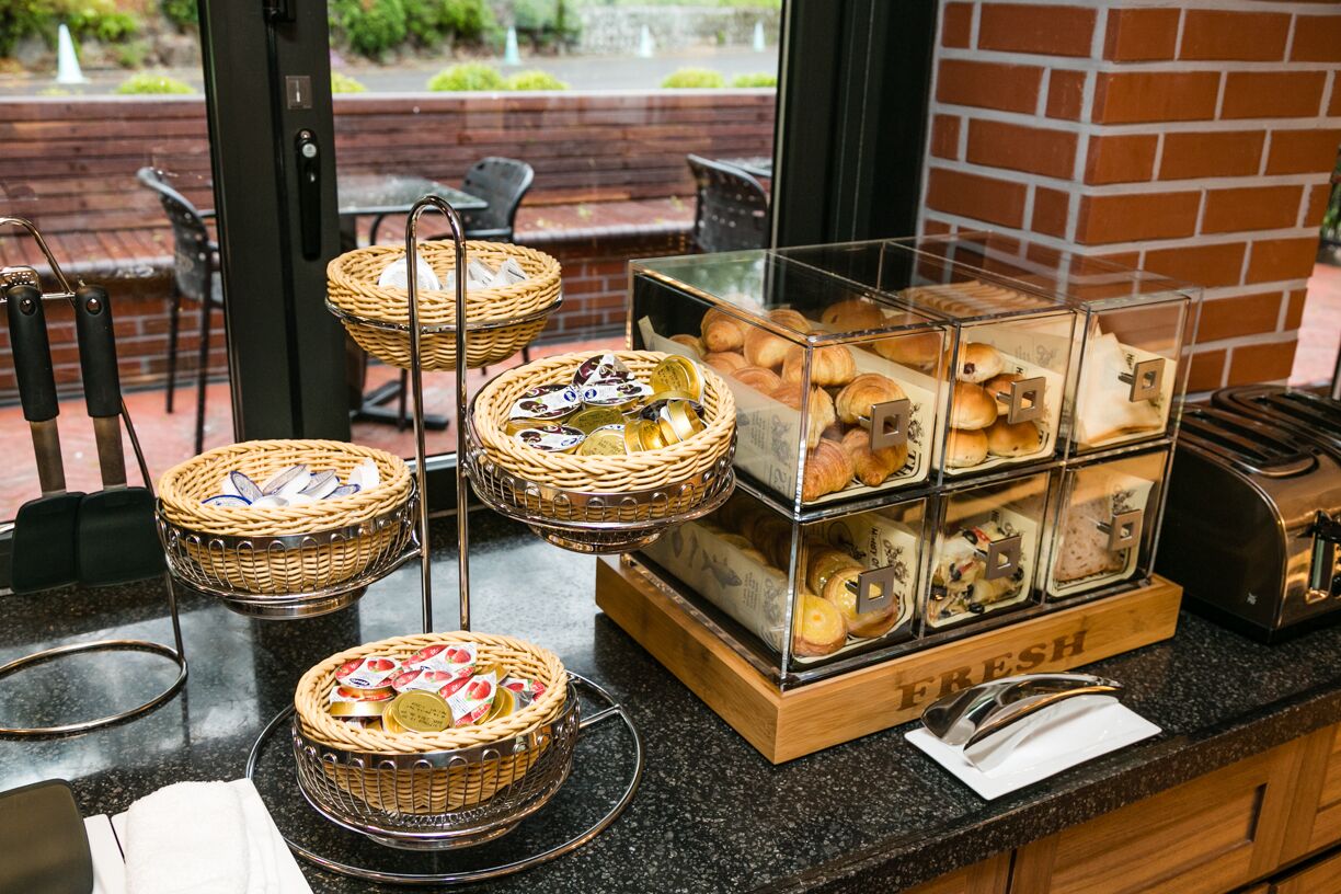 Ein Frühstücksbuffet mit Korbmöbeln und einer Glastheke mit der Aufschrift 'FRESH'.