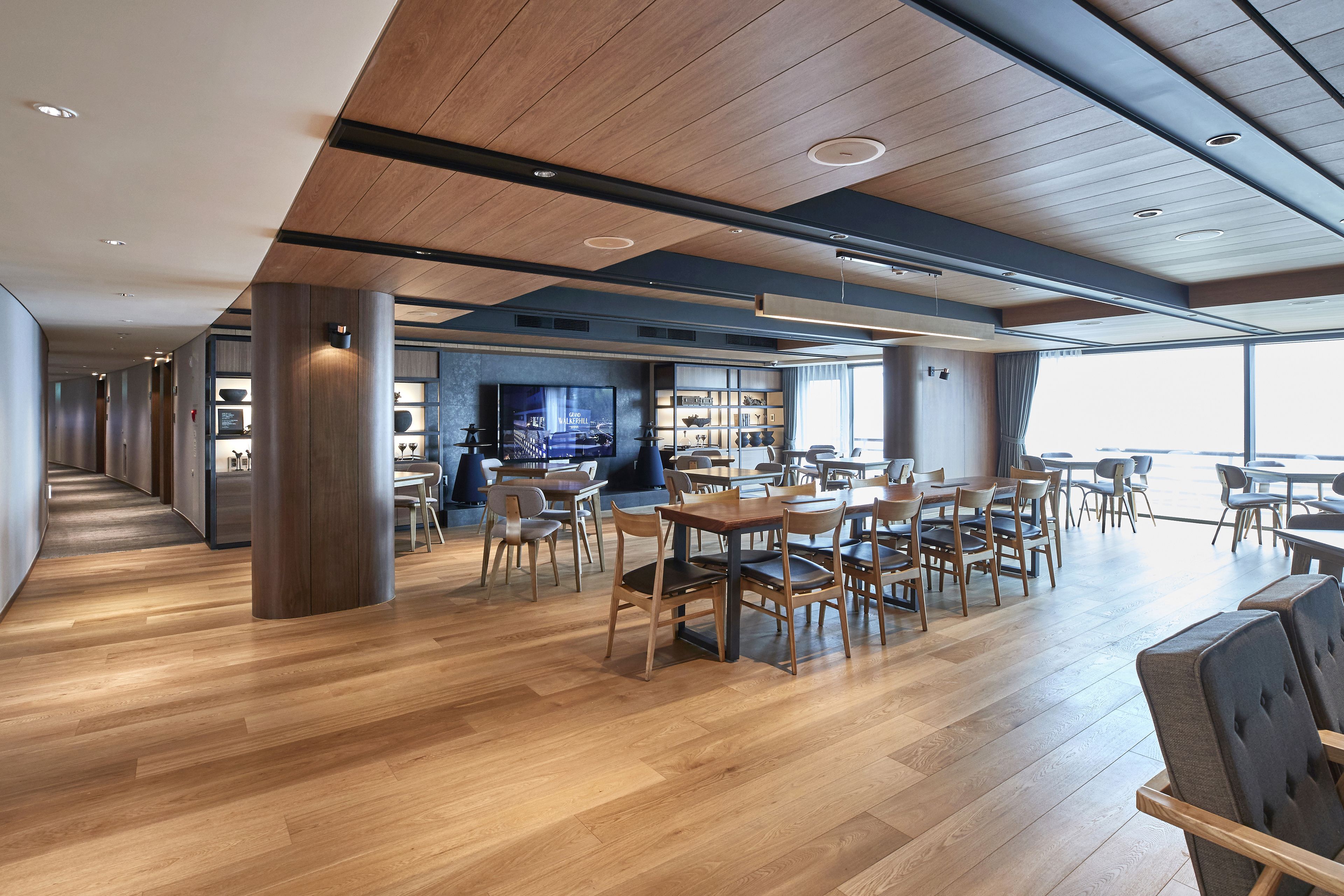 A spacious indoor area with wooden flooring, multiple seating arrangements, and a large window providing natural light.