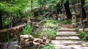 A stone pathway leading through a lush garden with a small stream and a stone lantern. - Walkerhill Douglas House (Seoul)