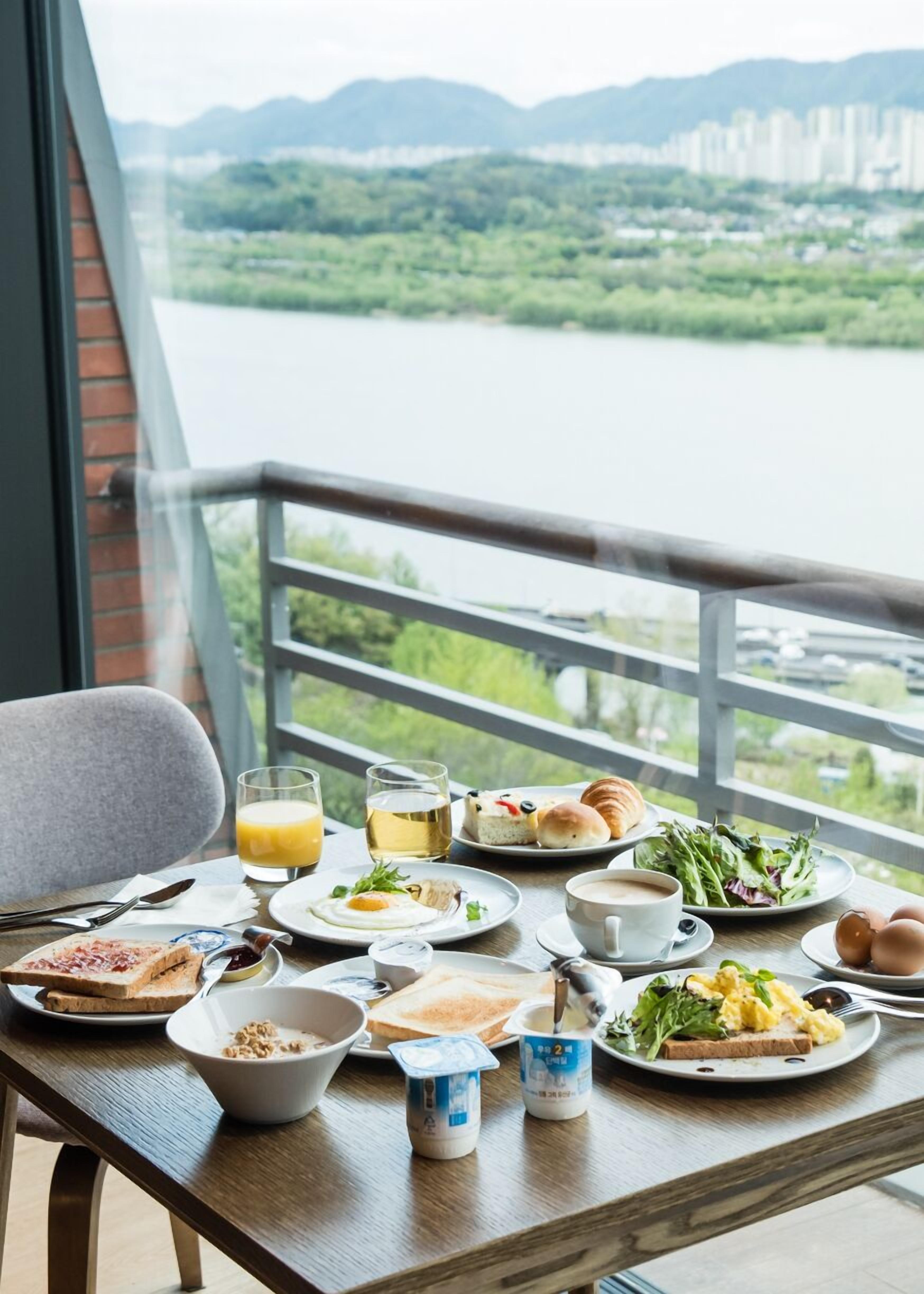 A dining table with breakfast items and a view of a river and mountains.