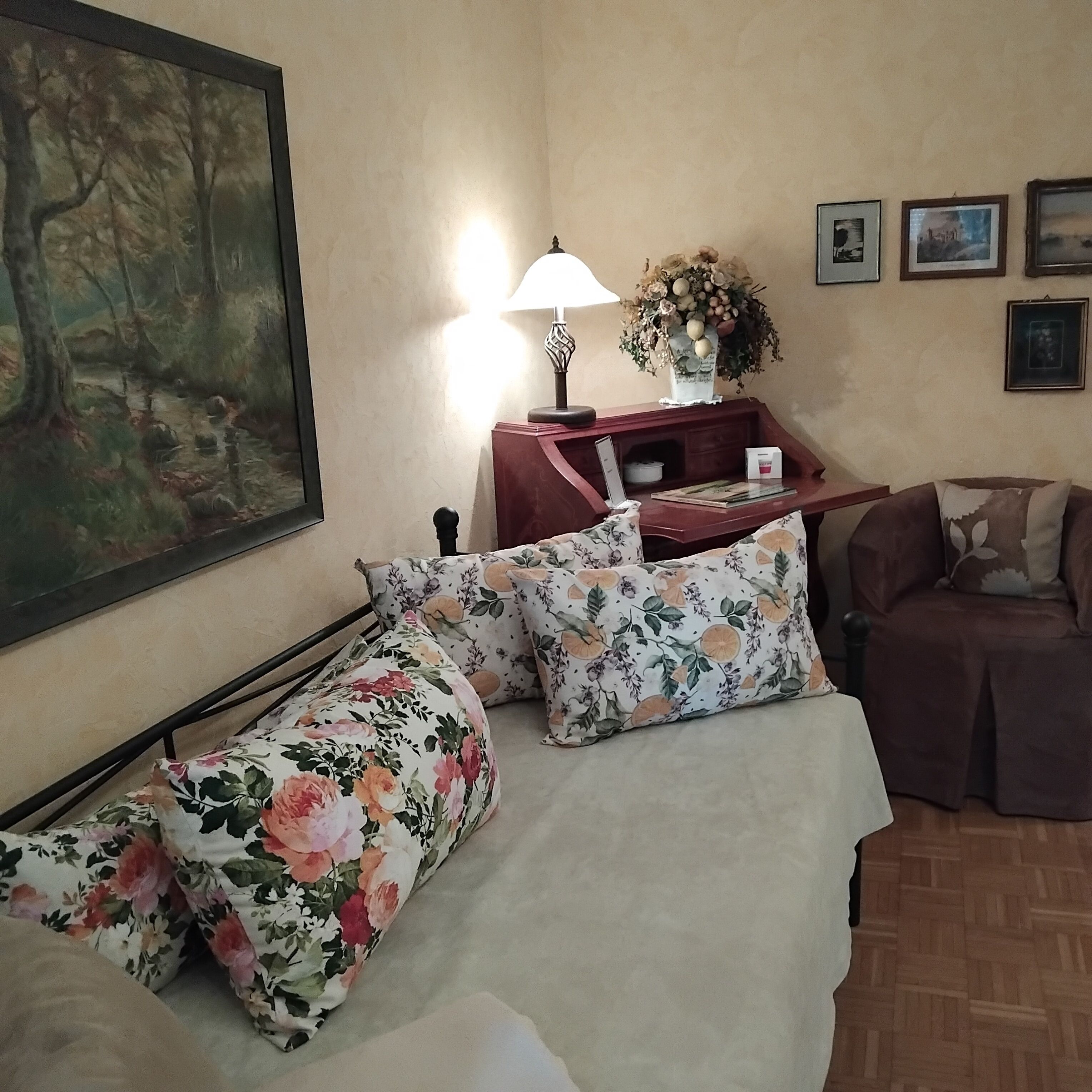 A bedroom with a bed, a nightstand, a lamp, a vase with flowers, and a painting on the wall.