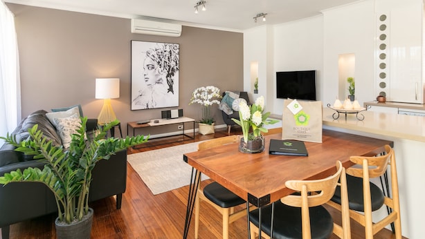 A modern living room with a wooden dining table, black and wooden chairs, a black sofa, a white lamp, and a large framed artwork on the wall. - BOUTIQUE STAYS - Sandy Breeze 3 (Sandringham)