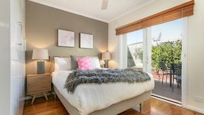 A bedroom with a bed, bedside lamps, a nightstand, and a view of the outdoors. - BOUTIQUE STAYS - Sandy Breeze 3 (Sandringham)