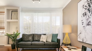 A modern living room with a leather sofa, a side table, a lamp, and a large abstract painting on the wall. - BOUTIQUE STAYS - Sandy Breeze 3 (Sandringham)
