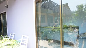 A glass door leading to a patio area with chairs and potted plants. - Kedsila Hometel (Pathio)