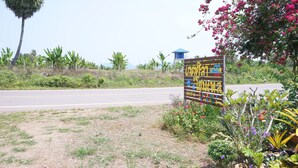 A signboard with text and symbols, surrounded by greenery and a road. - Kedsila Hometel (Pathio)