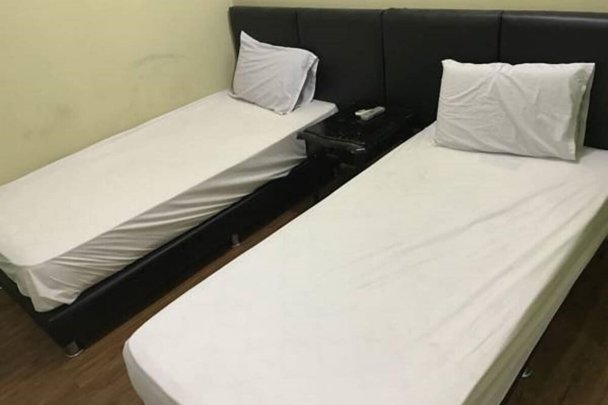 Dos camas individuales con sábanas y almohadas blancas, un cabecero negro y una mesita de noche con un control remoto.