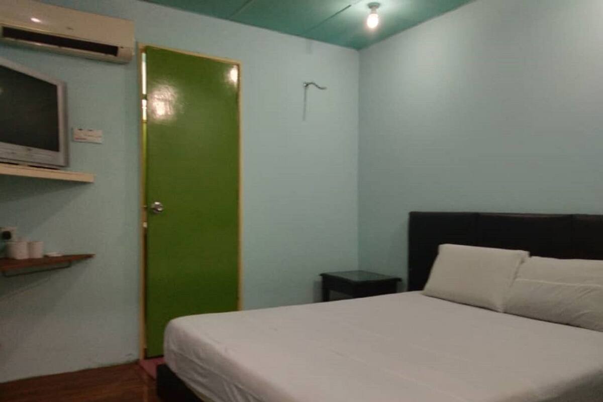 Een slaapkamer met een bed, een groene deur, een klein nachtkastje en een plank met toiletartikelen.