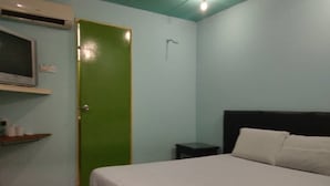 A bedroom with a bed, a green door, a small nightstand, and a shelf with toiletries.