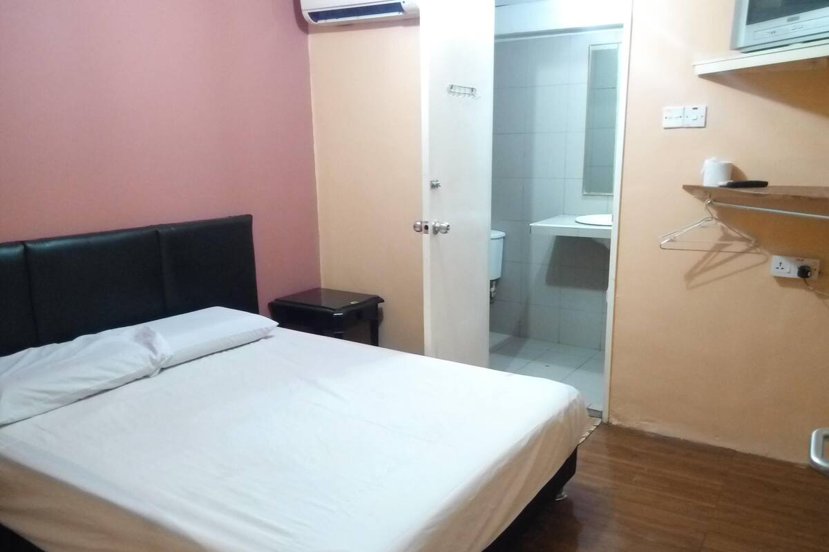 Een slaapkamer met een bed, een nachtkastje, een deur naar een badkamer en een plank met een hangend voorwerp.