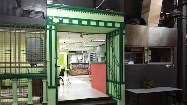A restaurant with a green entrance, a reception desk, and a seating area with tables and chairs.