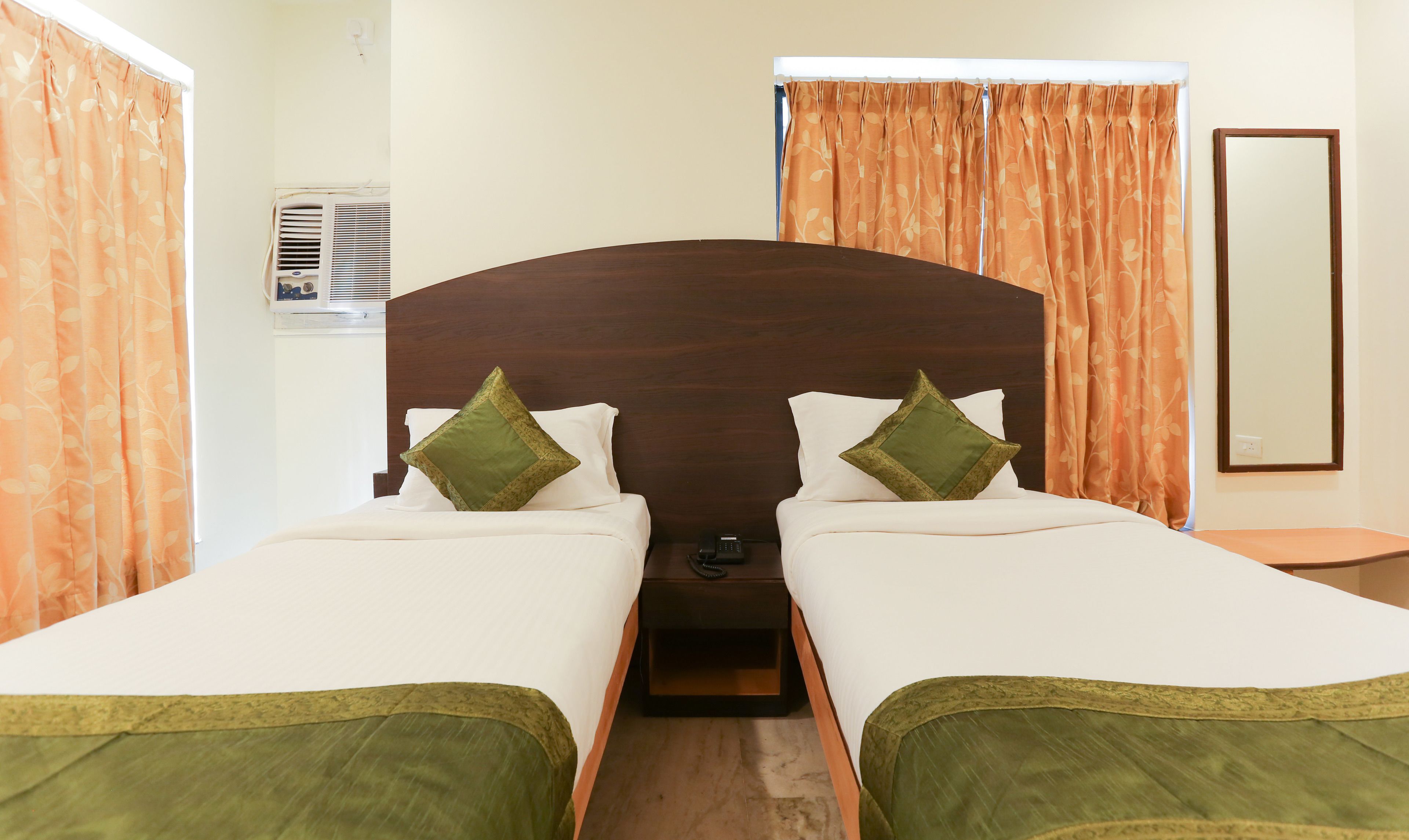 Habitación doble con dos camas, cada una con almohadas verdes, cabecero de madera y mesita de noche con teléfono.