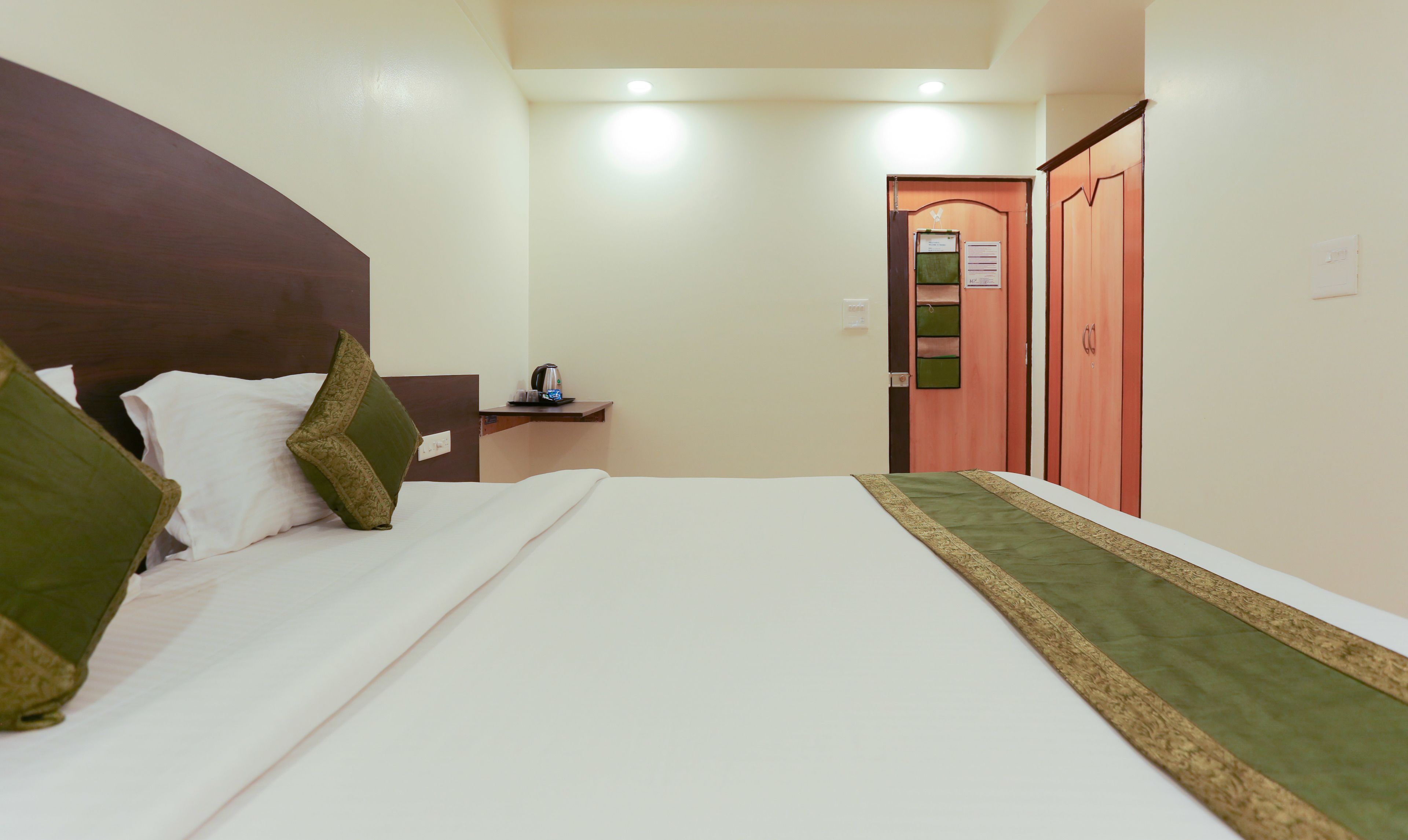 A hotel room with a bed, pillows, a nightstand, a coffee maker, and a door with a sign.