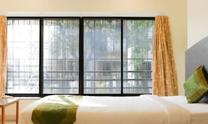 A hotel room with a large window, a bed with green and beige bedding, and a green pillow. - Itsy Hotels Hill View Ex (Pune)