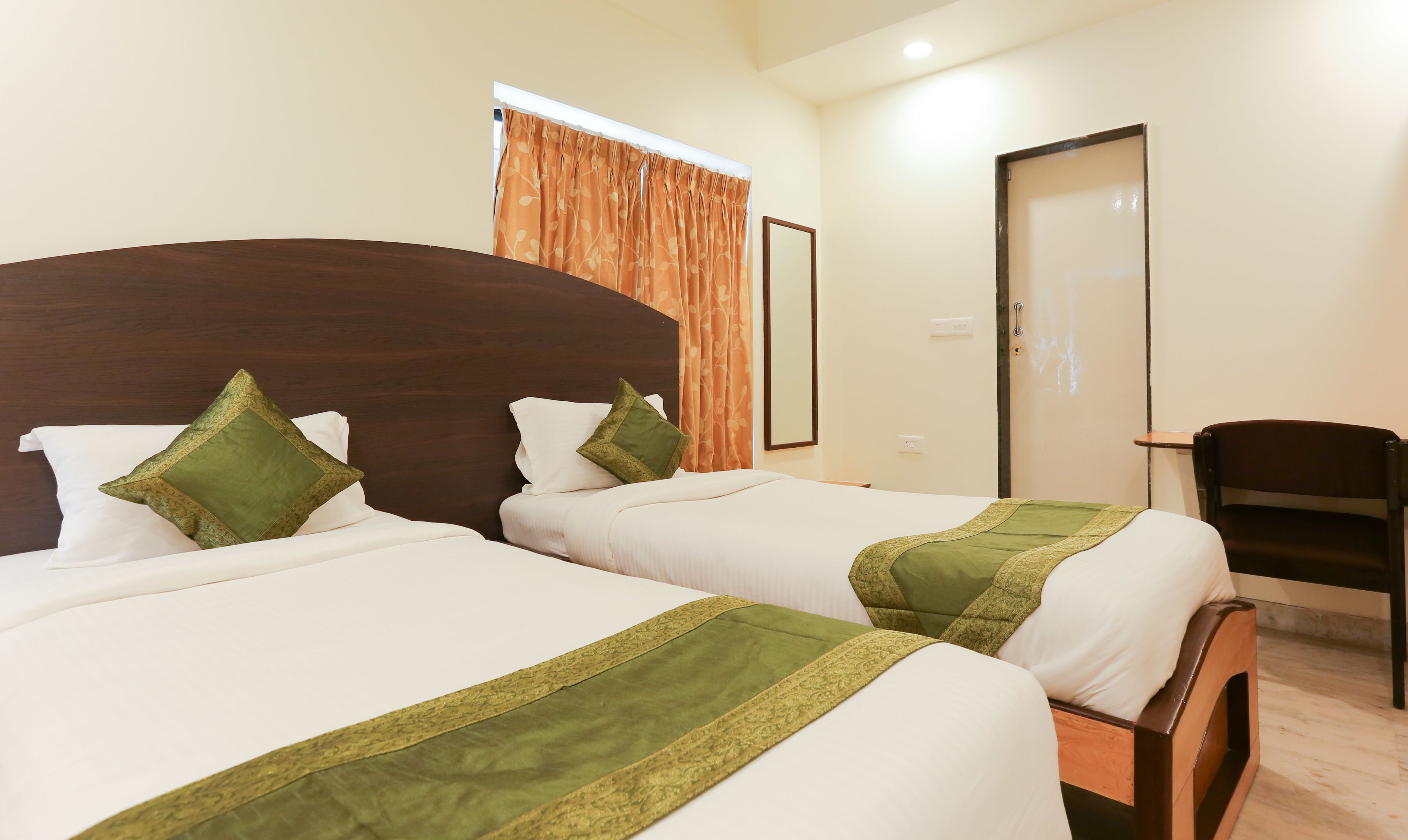 Ein Hotelzimmer mit zwei Betten, jeweils mit einem hölzernen Kopfteil und grünen Zierkissen.