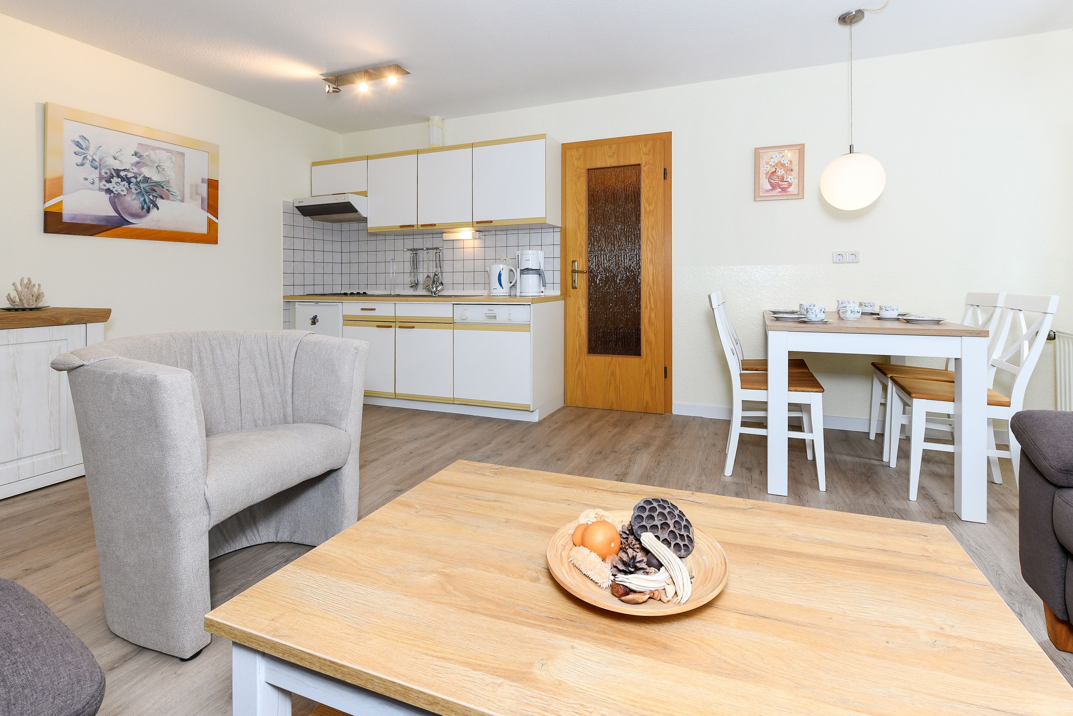 Una cocina moderna con armarios blancos, una puerta de madera y un comedor con sillas blancas y una mesa de madera.