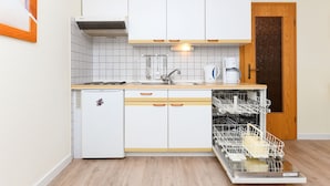Et kompakt køkken med hvide skabe, en indbygget opvaskemaskine og et lille køleskab.