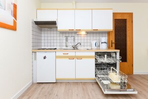 Une cuisine compacte avec des meubles blancs, un lave-vaisselle intégré et un petit réfrigérateur.