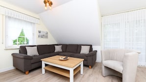 En moderne stue med en mørkegrå hjørnesofa, et lyst træ sofabord og en lysegrå lænestol.