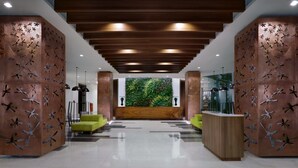 Un hall d’entrée moderne avec un comptoir d’accueil en bois, des sièges verts et un mur végétal.