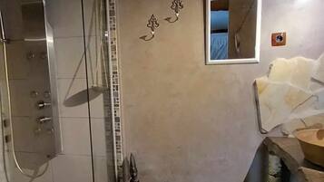 A bathroom with a glass shower enclosure, a small mirror, and a towel rack.