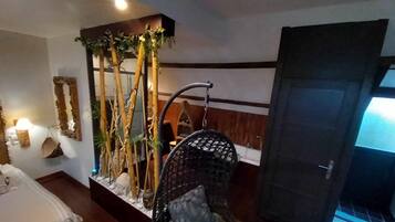 A room with a bed, a wall-mounted lamp, a hanging chair, and a door with a window.