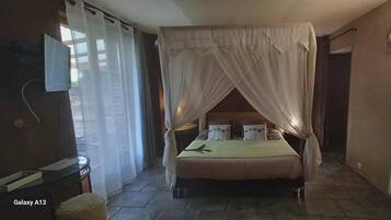 A bedroom with a bed under a canopy, a bedside table, a chair, a radiator, and a window with curtains.
