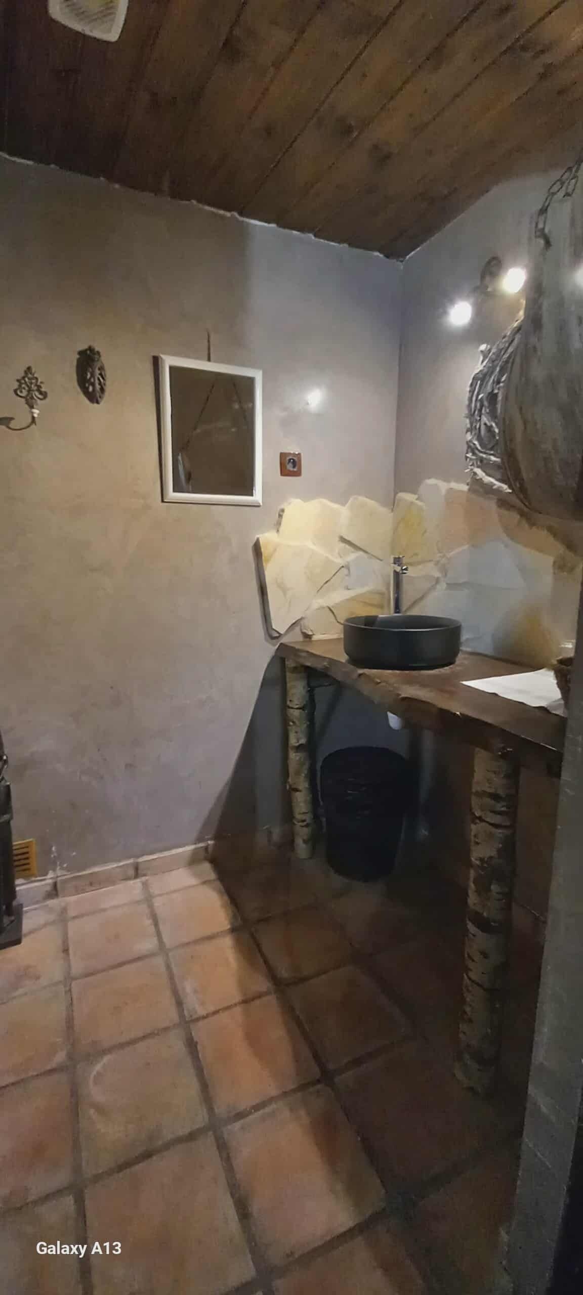 A small, rustic kitchen with a stone wall, a wooden ceiling, and a tiled floor.