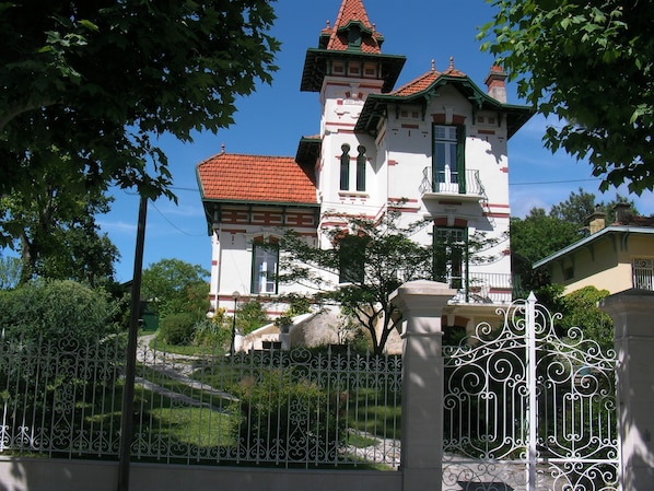 A white building with a red roof and green accents, surrounded by trees and a white wrought iron fence. - 3-star apartment in Arcachon house (Arcachon)
