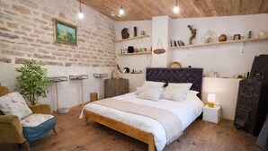 Un dormitorio con una cama de madera, una silla, una planta y estantes con diversos objetos.