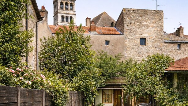 Un jardín con un muro de piedra, una valla de madera y un camino que lleva a un edificio con una torre.