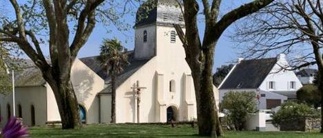 Uma igreja com um campanário, rodeada por árvores e um espaço gramado.
