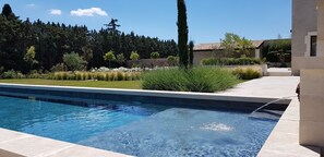Ein Schwimmbecken mit klarer, blauer Wasseroberfläche, umgeben von einem gepflegten Garten mit verschiedenen Pflanzen und Bäumen.