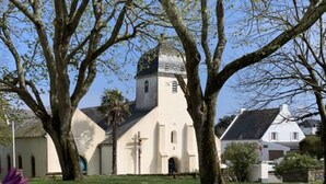 Una iglesia con un campanario, rodeada de árboles y un césped.