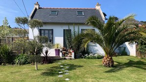 Une maison à l’extérieur blanc, avec un toit gris et un jardin agrémenté d’un chemin de pierre menant à l’entrée.