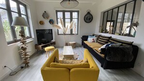 Un salon avec un canapé jaune, un téléviseur, une table basse et une grande fenêtre.